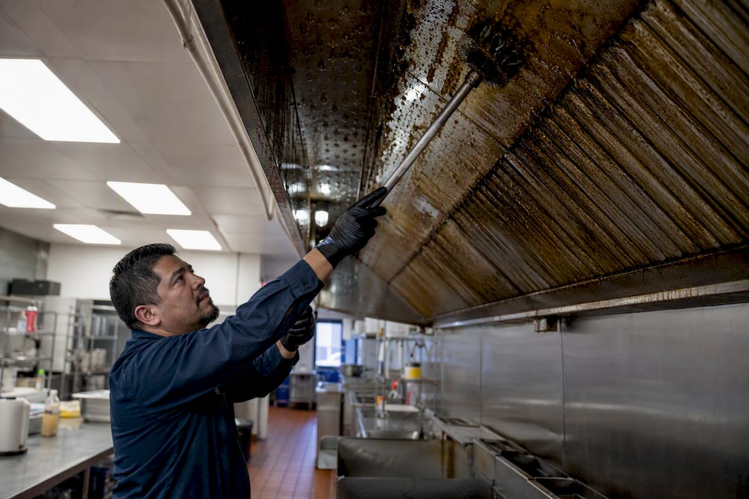 Technician degreasing kitchen exhaust duct