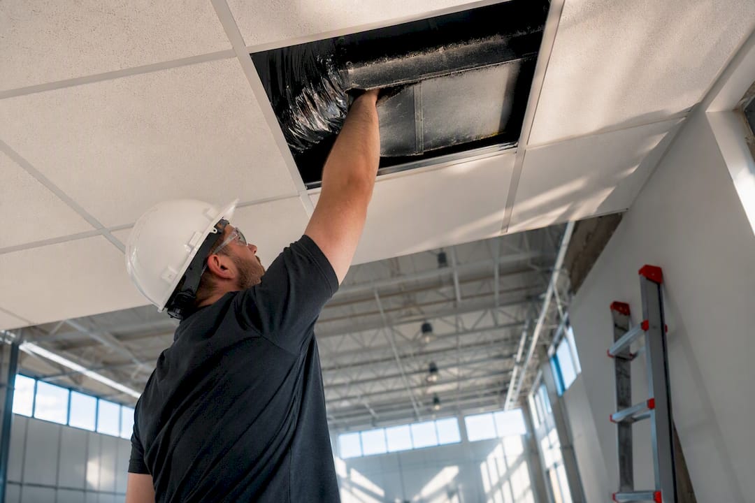 Technician accessing duct above drop ceiling