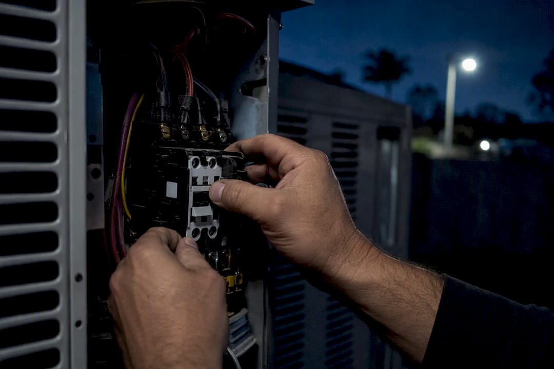 Hands replacing AC electrical part at night
